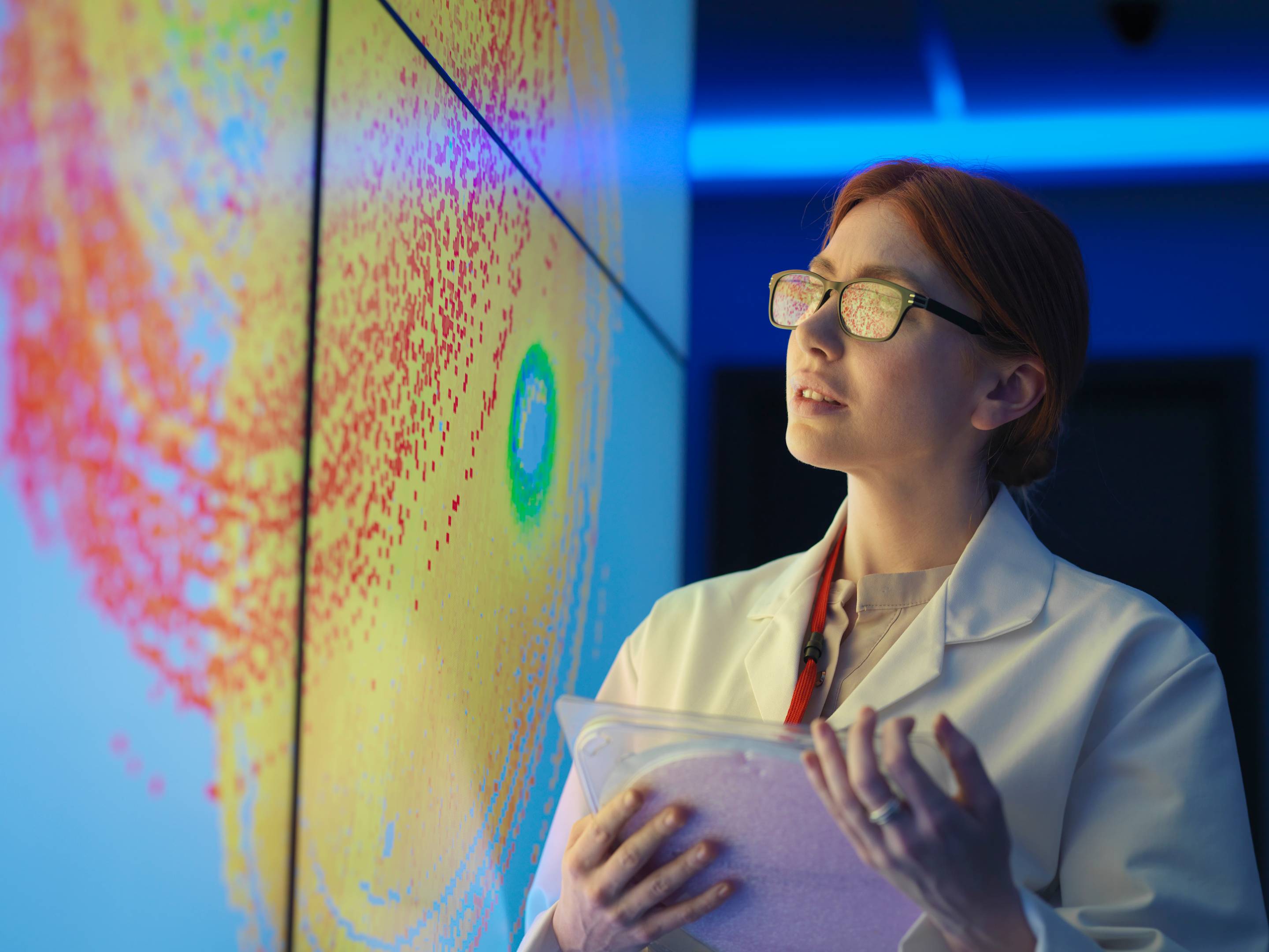 Female scientist with silicon wafer studying graphical display of wafer on screens